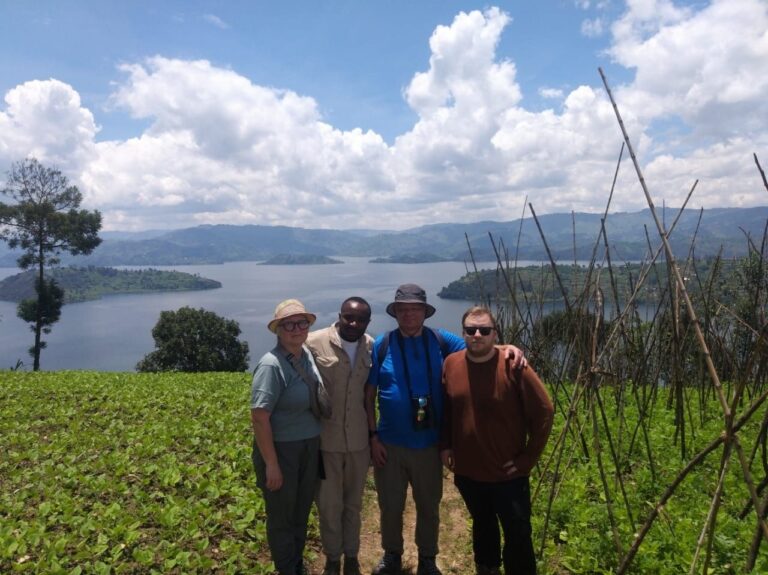 Group of four visitors standing on a hilltop overlooking a large lake and green hills